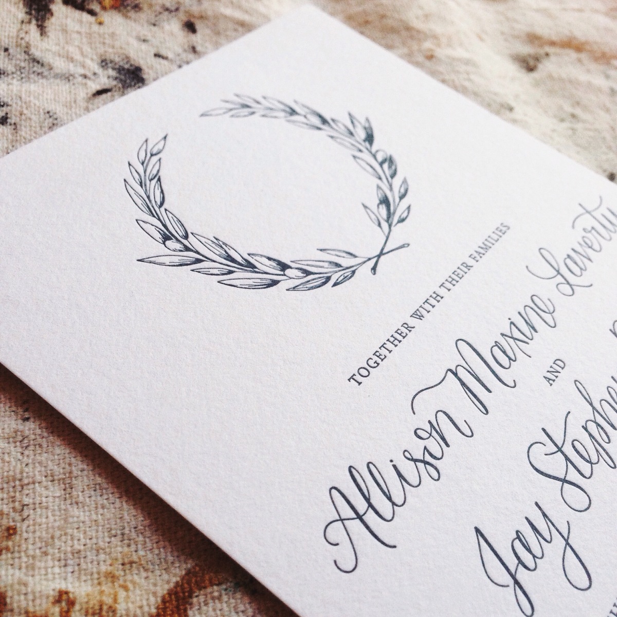 - AMY ROCHELLE PRESS - Detail view of olive crest and modern calligraphy on letterpress wedding invitation.